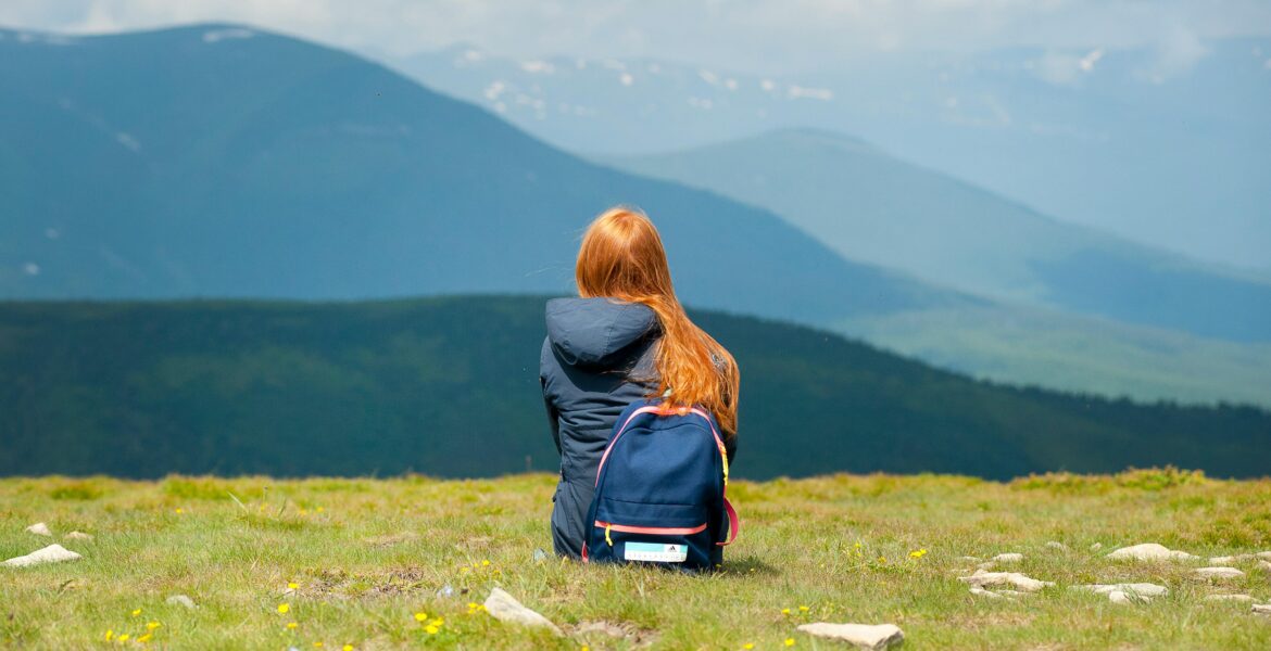 A woman sits on a grassy hilltop with a breathtaking mountain view, enjoying a peaceful moment in nature.