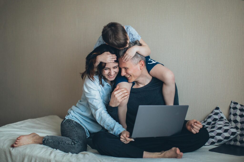 Family of three sitting on the bed, father using a laptop, mother and son beside him, symbolizing family connection