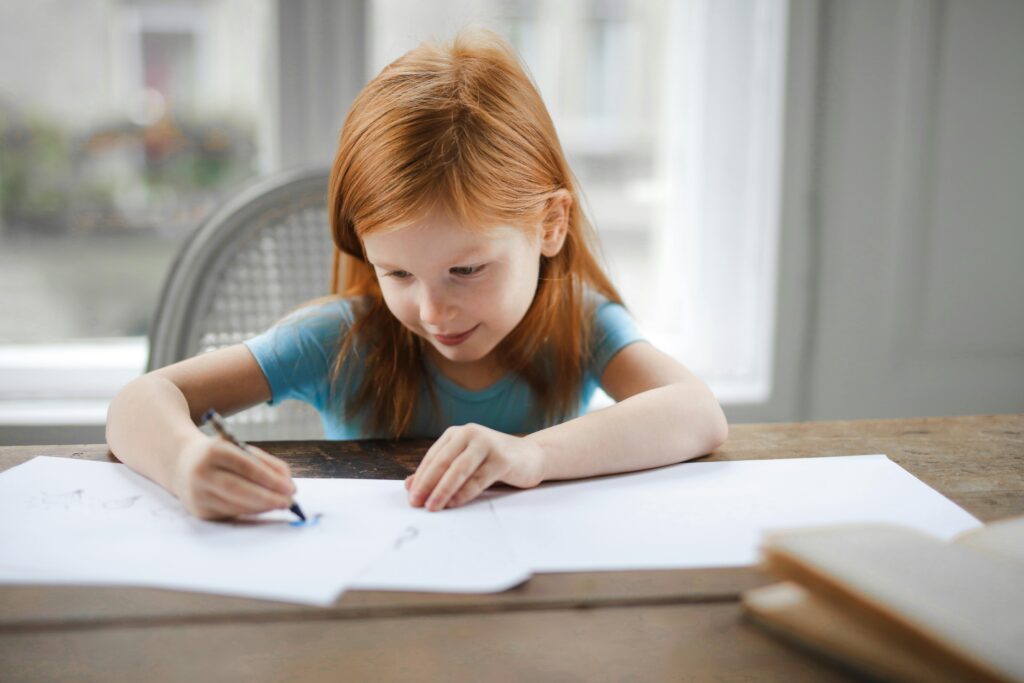 Red-haired girl doing homework at a table, symbolizing focus, learning, and academic engagement Therapy for children in Blaine MN