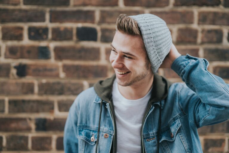 Teenage boy wearing a gray beanie and jean jacket, smiling while standing in front of a brick wall, symbolizing youth, confidence, and casual style. Therapy for depression in Blaine MN