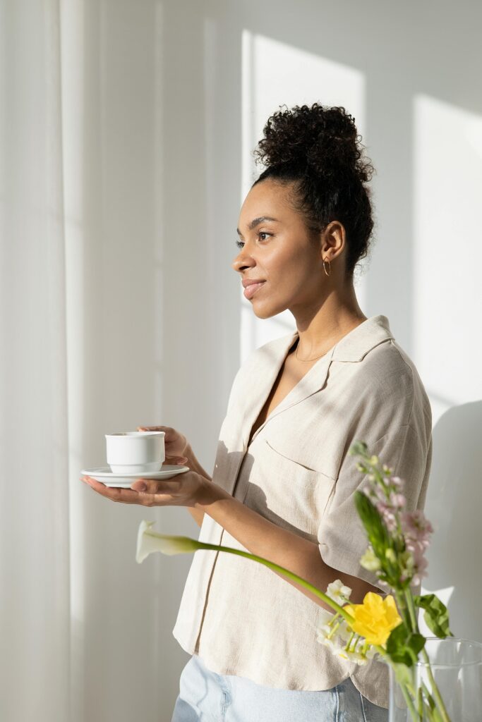 Woman looking out a window with a peaceful expression while holding a cup of coffee, symbolizing calm and mindfulness
