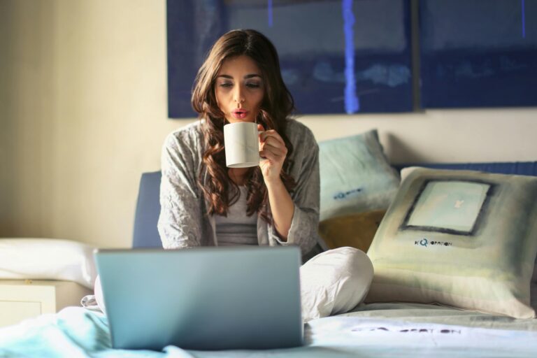 Woman on her bed with her laptop open and drinking a cup of coffee, symbolizing comfort, focus, and reflection Therapy in Blaine MN