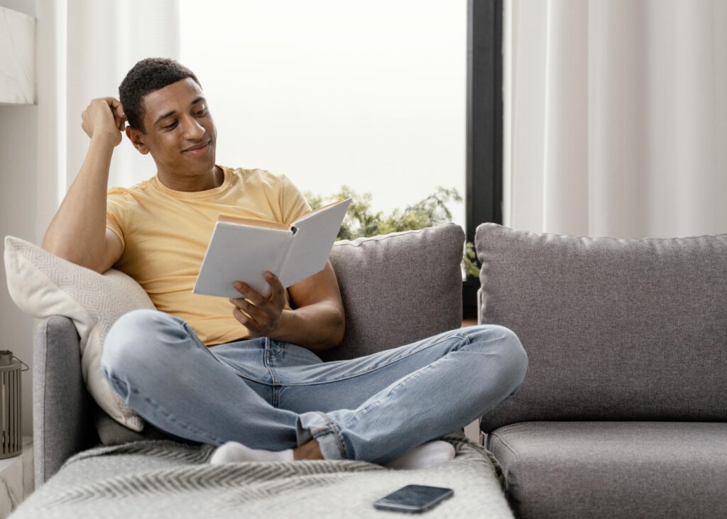Young man reading a book on a couch with his legs folded, symbolizing relaxation and focused learning Therapy For Self Esteem in Blaine MN