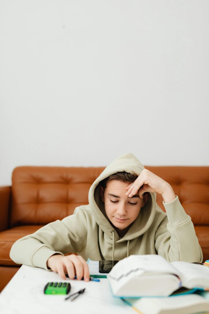 Teenager in a hoodie studying at home with books and calculator on the table. Therapy for academic stress in blaine mn