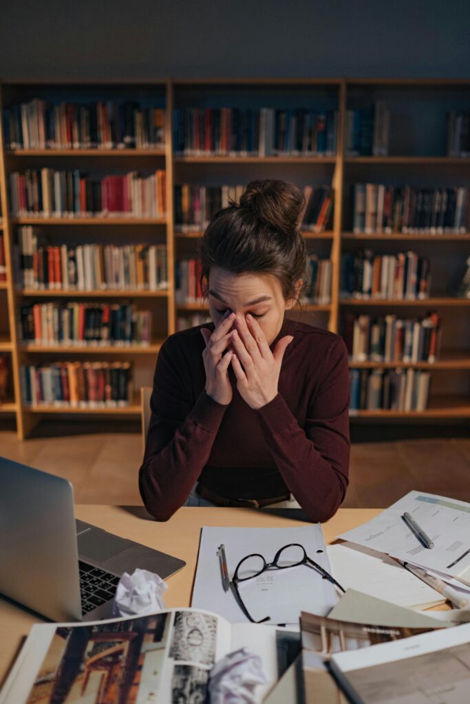 Woman feeling stressed while studying in a library, surrounded by books and laptop. Therapy for life transitions in Blaine MN