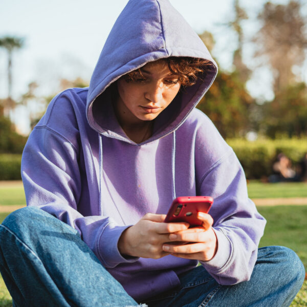 Bored teenager using a mobile phone in the park. She is sitting in the grass.