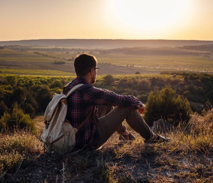 Hiker with backpack sitting on top of the mountain. Orange daybreak at horizon. Lifestyle hiking concept, summer vacations outdoor