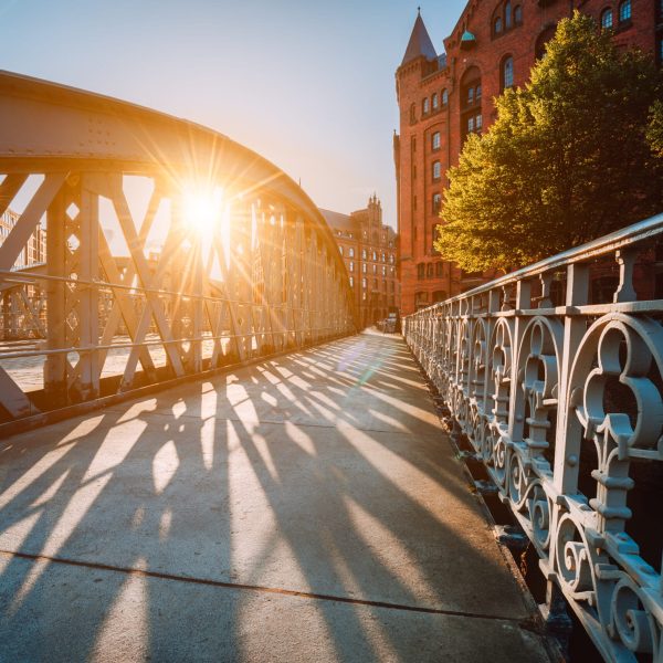 Metal arch bridge in the Speicherstadt of Hamburg with sunburst light during sunset golden hour.