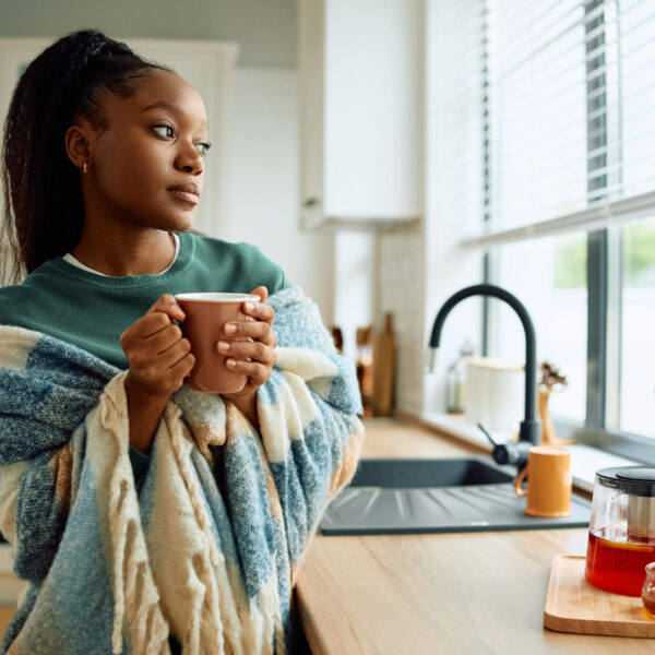 African American woman with cup of tea looking through the window from her kitchen. Copy space.