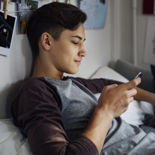 Teenage boy using smartphone in a bedroom social media concept