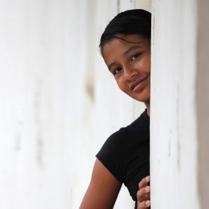 Teenage girl looking around the corner smiling at the camera Therapy in Blaine MN