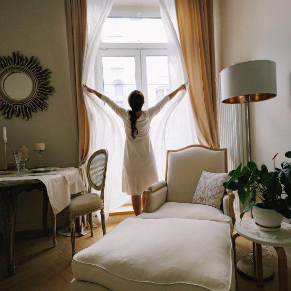 Woman standing in her living room, opening curtains and looking out the window, embracing a new day and fresh start