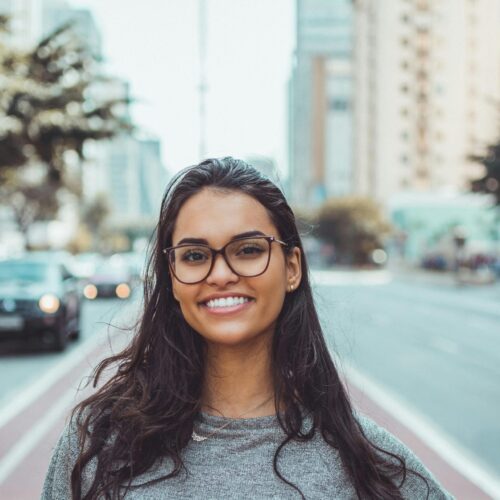 Woman with glasses standing in a busy city street, smiling at the camera, symbolizing confidence and positivity Therapy for adults in Blaine MN